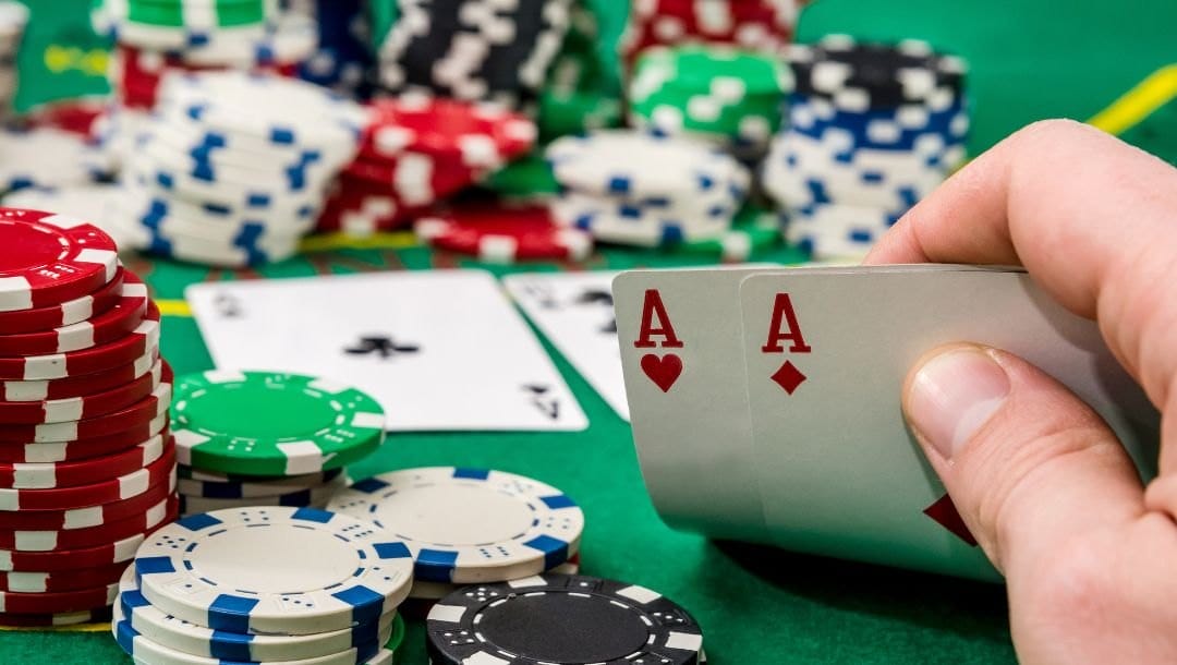 A hand revealing an Ace of Hearts, and an Ace of Diamonds at a poker table with more playing cards, and poker chips arranged on the table.