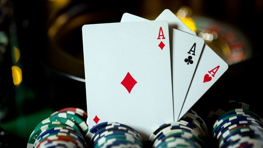 An Ace of Diamonds, an Ace of Spades, and an Ace of Hearts, arranged on top of poker chips.