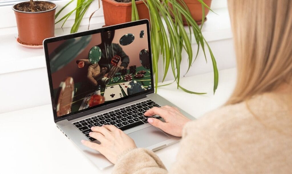 An over-the-shoulder view of a woman visiting an online poker website on her laptop.