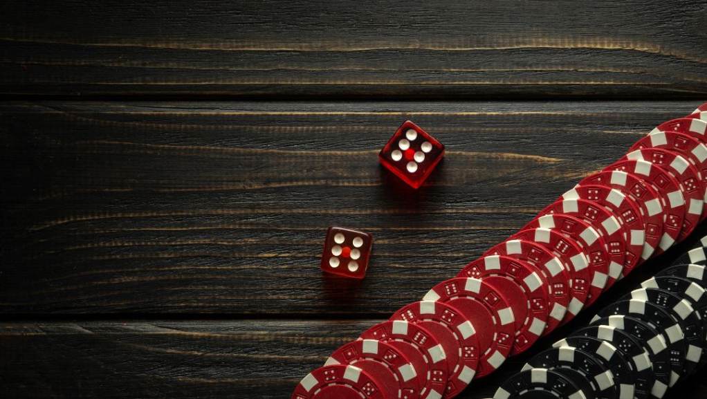 Two red six-sided dice and two rows of poker chips, one black and one red row, on top of a dark wooden surface.