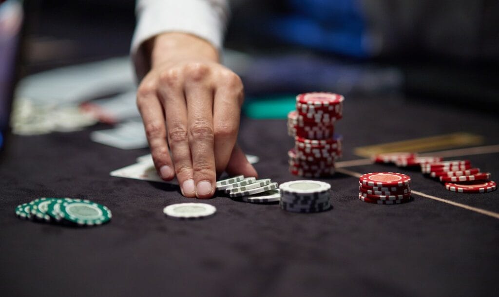 A hand picking up casino chips on a black felt table.