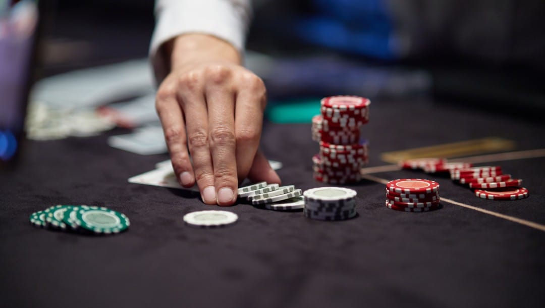 A hand picking up casino chips on a black felt table.