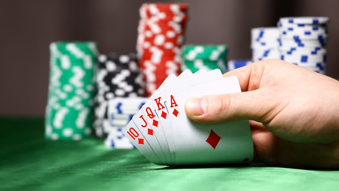 A hand holding playing cards with casino chips in the background.