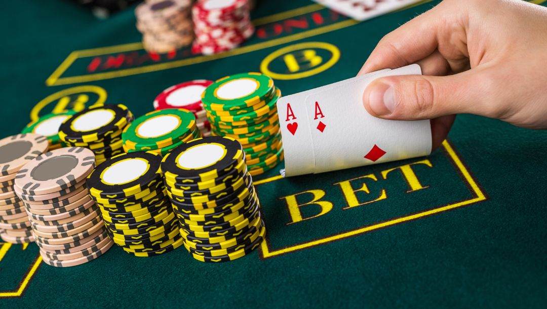 Hand displaying cards at a poker table, revealing an Ace of Hearts and an Ace of Diamonds, surrounded by poker chips.
