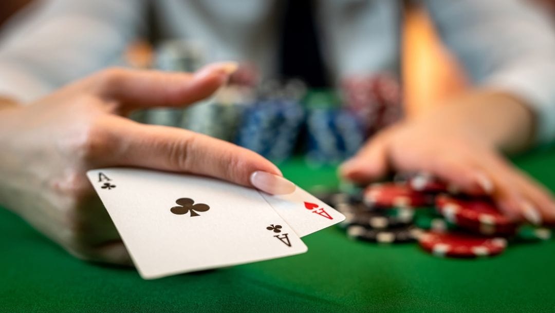 Hand displaying cards at a poker table, revealing an Ace of Hearts and an Ace of Clubs, surrounded by poker chips.