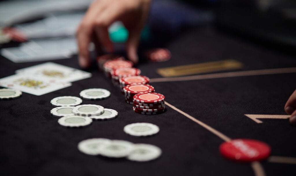 A hand picking up red poker chips on a black poker table.