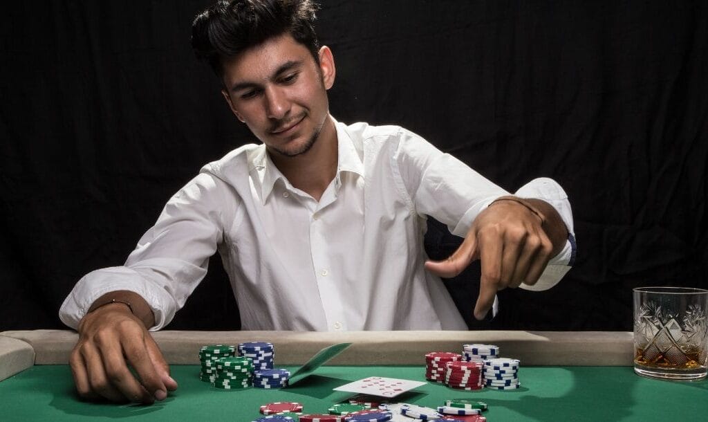 A man in action at a poker table, tossing playing cards down, with casino chips neatly arranged in front of him.
