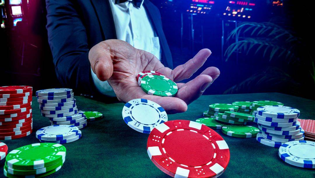 A person's hand, throwing casino chips onto a poker table, with more casino chips arranged on the poker table.