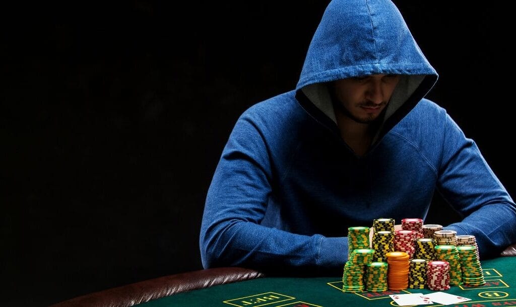 A man in a blue hoodie seated at a poker table, with a stack of cards and casino chips neatly arranged in front of him.