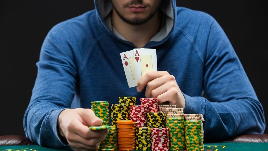 A man in a blue hoodie seated at a poker table, with a stack of cards and casino chips neatly arranged in front of him.