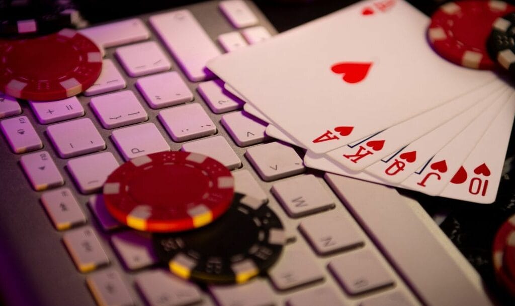 a royal flush of hearts playing cards and red and black poker chips on a computer keyboard