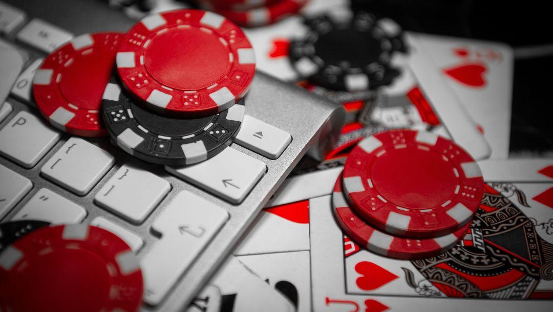 red and black poker chips and playing cards scattered on, under and around a computer keyboard