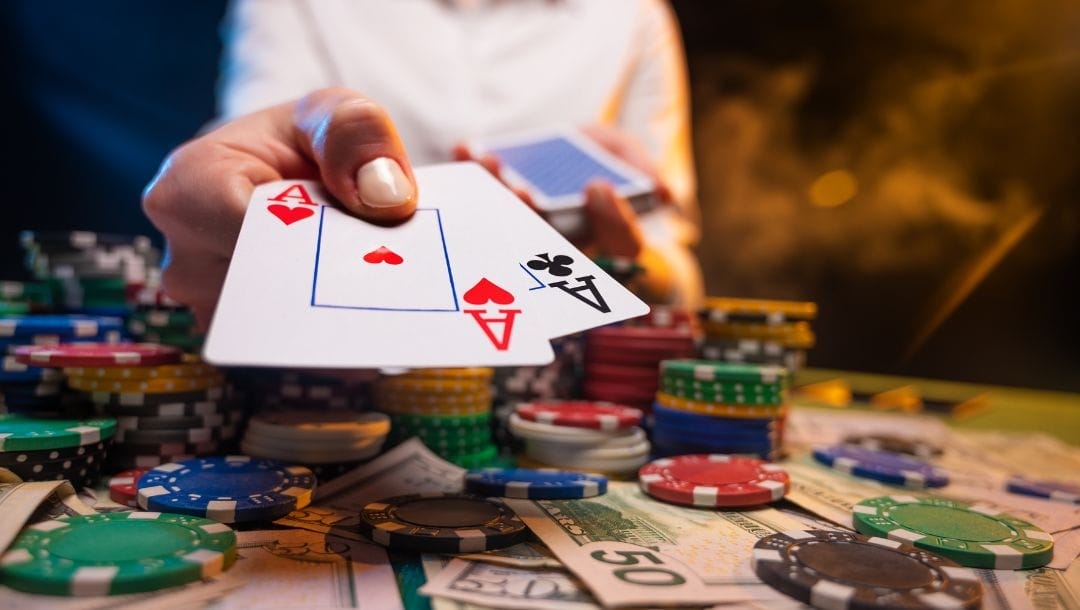 A dealer presenting two cards, an Ace of Hearts and an Ace of Clubs, with cash and casino chips arranged on the poker table.