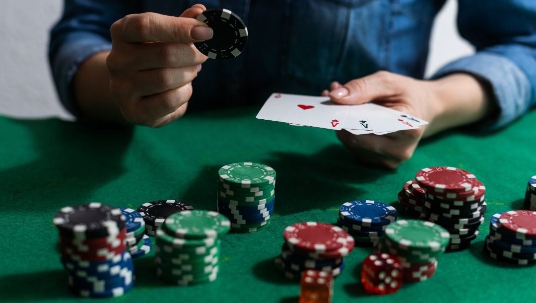 A person sitting at a poker table, holding a poker chip and playing cards, with poker chips arranged on the table.