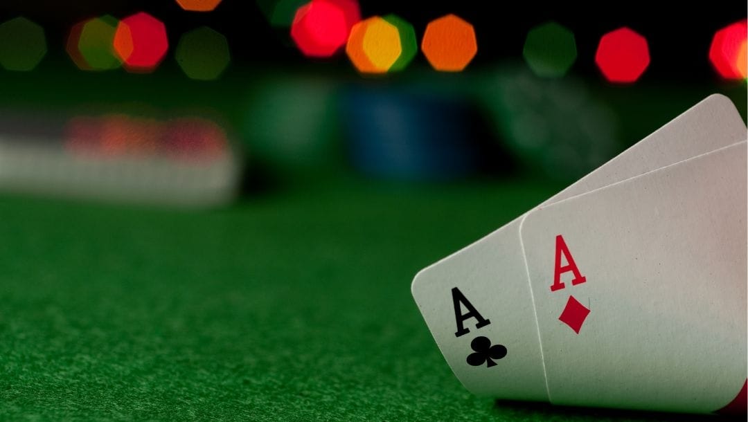 Hand displaying cards at a poker table, revealing an Ace of Diamonds and an Ace of Clubs.