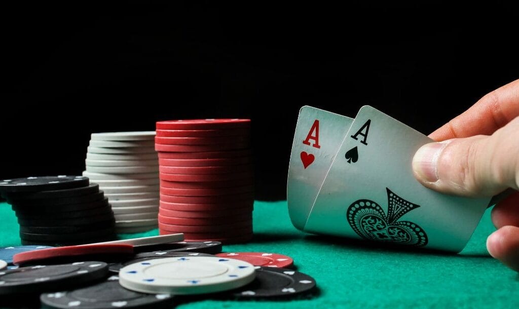 Hand displaying cards at a poker table, revealing an Ace of Hearts and an Ace of Spades, surrounded by poker chips.