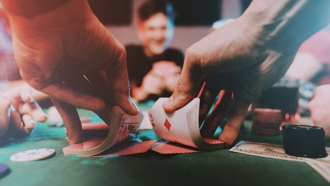 A dealers hands shuffling cards, at a poker table, dealing cards to players, with casino chips arranged on the table.
