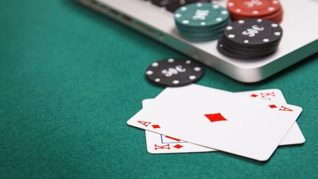 Cards and casino chips arranged on a poker table and a laptop.