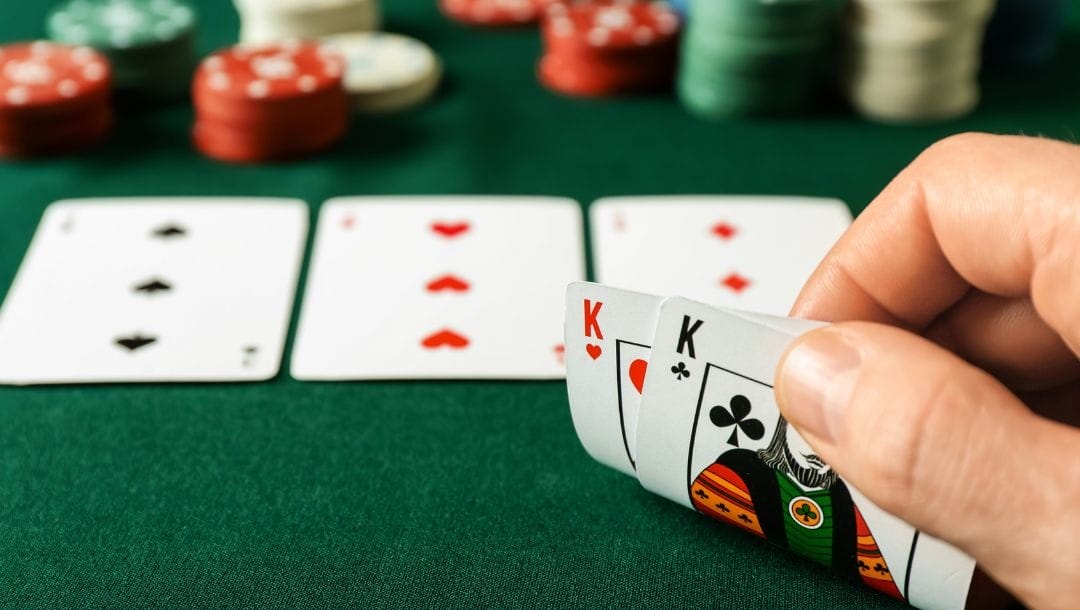 Player at a poker table confidently revealing their hand, showing a King of Hearts and a King of Clubs.