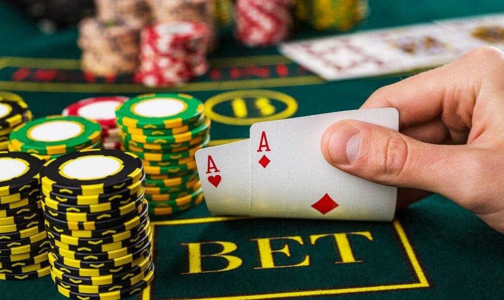 A poker player checking their hole cards next to multiple stacks of poker chips. They have two aces.