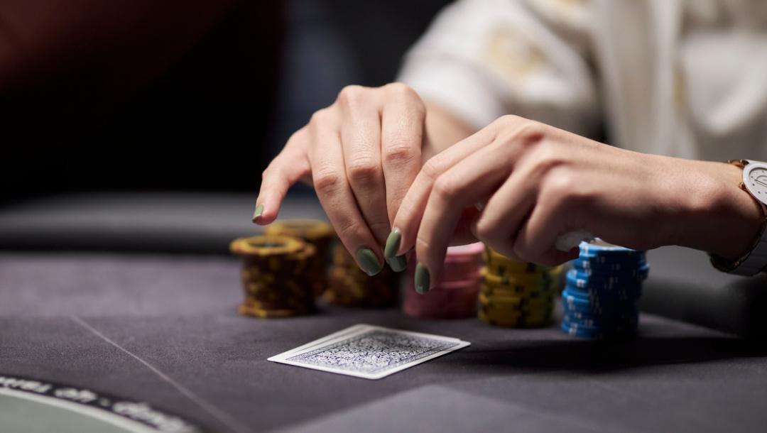 A woman with her hands above her cards at a poker table