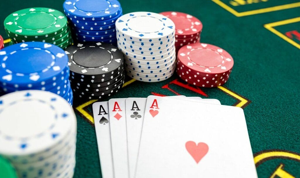 Four aces sitting on a casino table surrounded by stacks of poker chips.