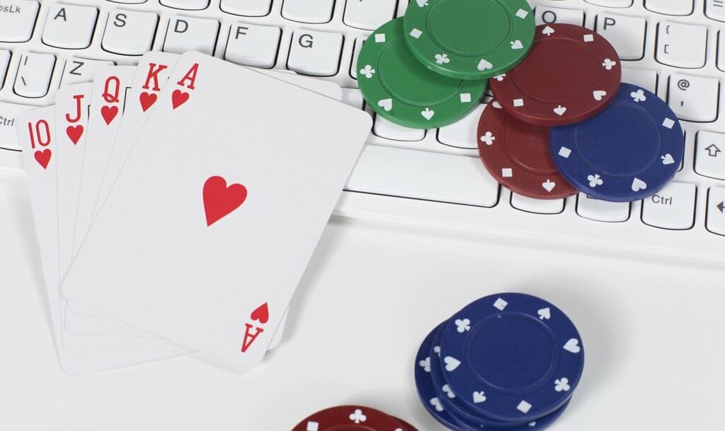 A royal flush sitting on a keyboard next to scattered poker chips.