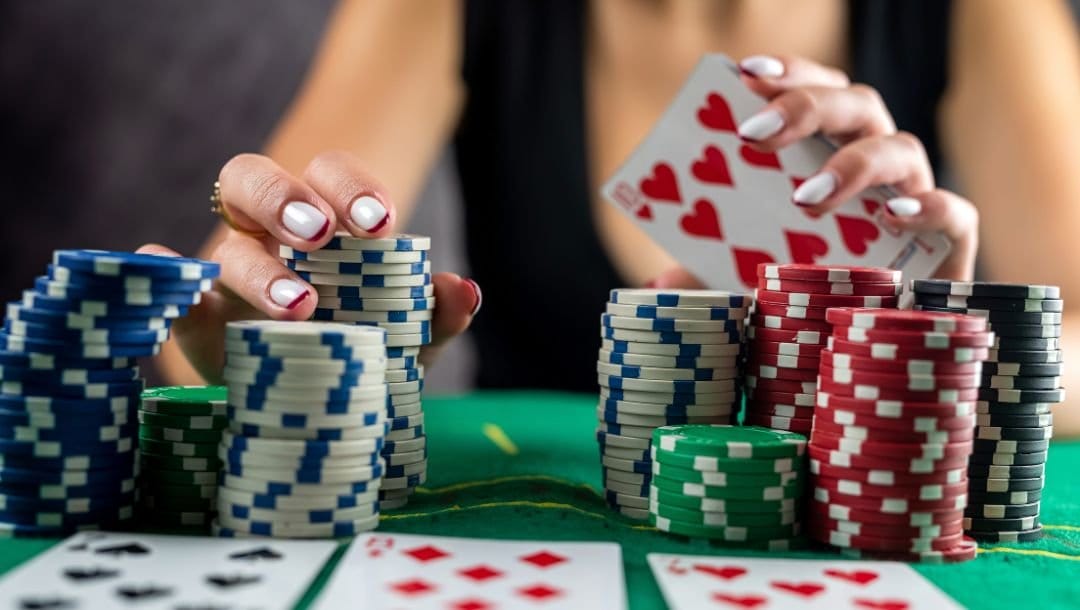 a woman is picking up from a stack of poker chips while showing her hole cards in the blurred background
