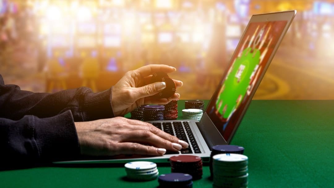 a person is playing online poker on a laptop with stacks of poker chips on either side of it on a green felt poker table in a casino