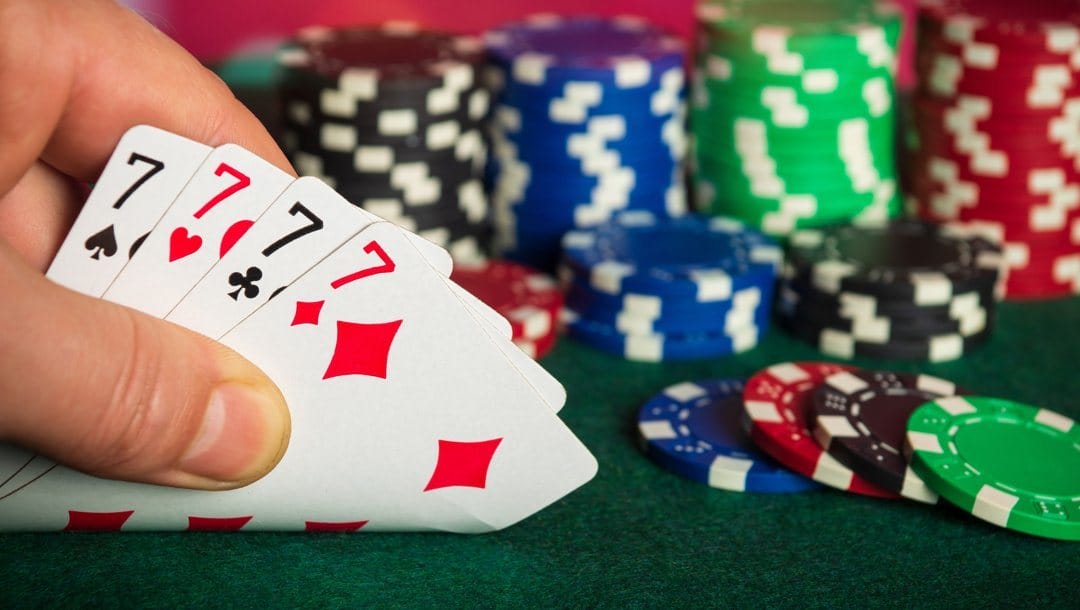 A PLO poker player looks at their hole cards. They have four 7s. There are poker chips in the background.
