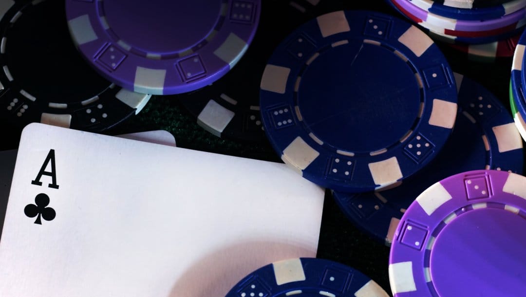 An ace of clubs sitting amongst scattered purple, blue, and black poker chips.