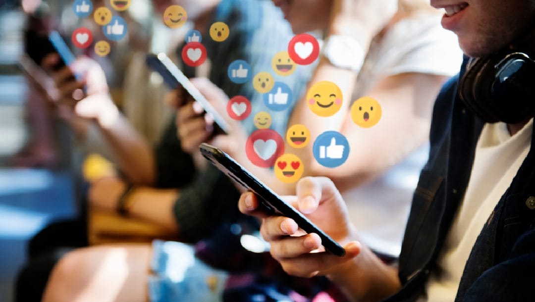 People with their phones out and different emojis floating out from the screens.