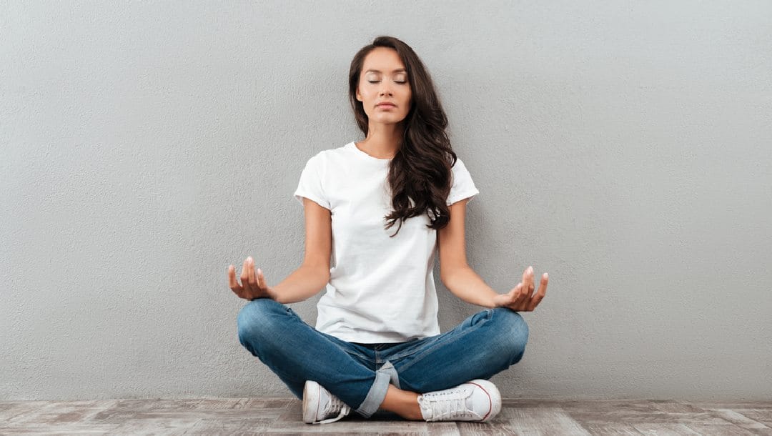 A person sits cross-legged against a wall and meditates.