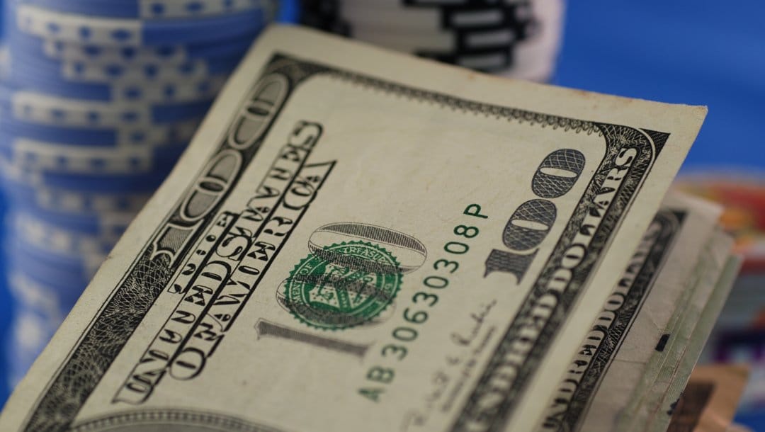 A close-up of $100 bills with stacks of poker chips in the background.
