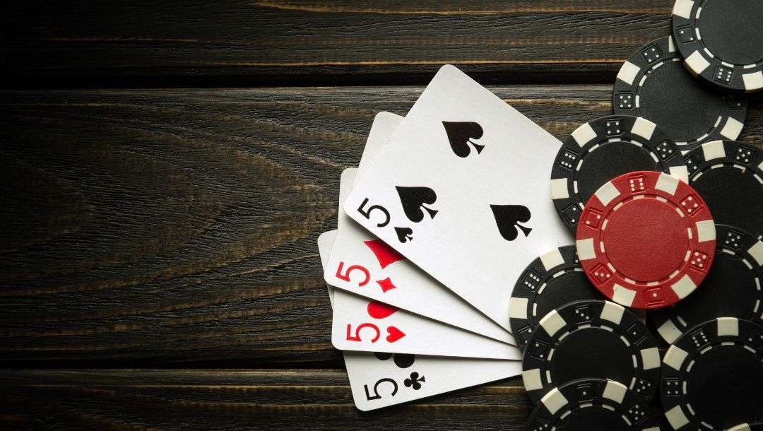 Four of a kind on a dark wooden table with poker chips fanned out on the right side of the image.