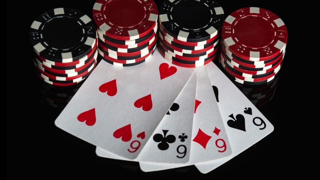 A top-down view of a four of a kind poker hand made up of sixes with four short stacks of poker chips weighing down the cards.