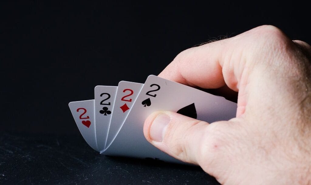 a person checking their playing cards of four of a kind two’s on a black surface