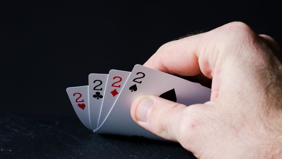 a person checking their playing cards of four of a kind two’s on a black surface