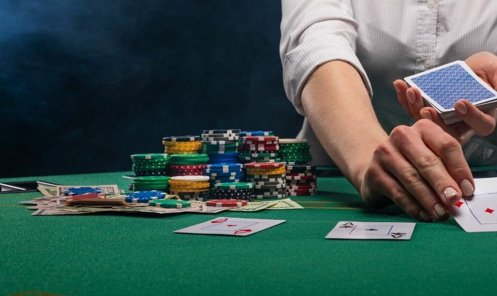 a poker dealer turning a playing card over on a green felt poker table during a game of poker with stacks of poker chips and money bills on the table
