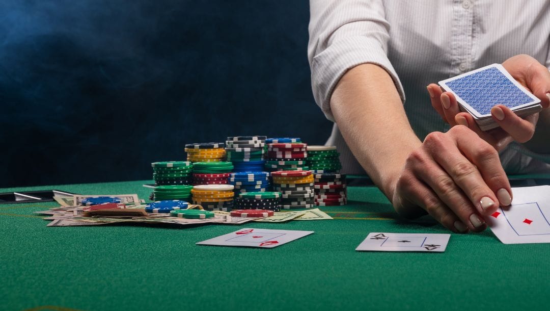 a poker dealer turning a playing card over on a green felt poker table during a game of poker with stacks of poker chips and money bills on the table