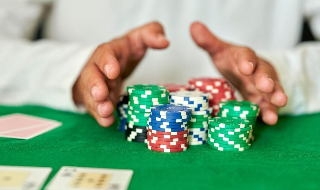 A person sitting at a poker table, pushing stacks of red, blue, green, white, and black poker chips forward.