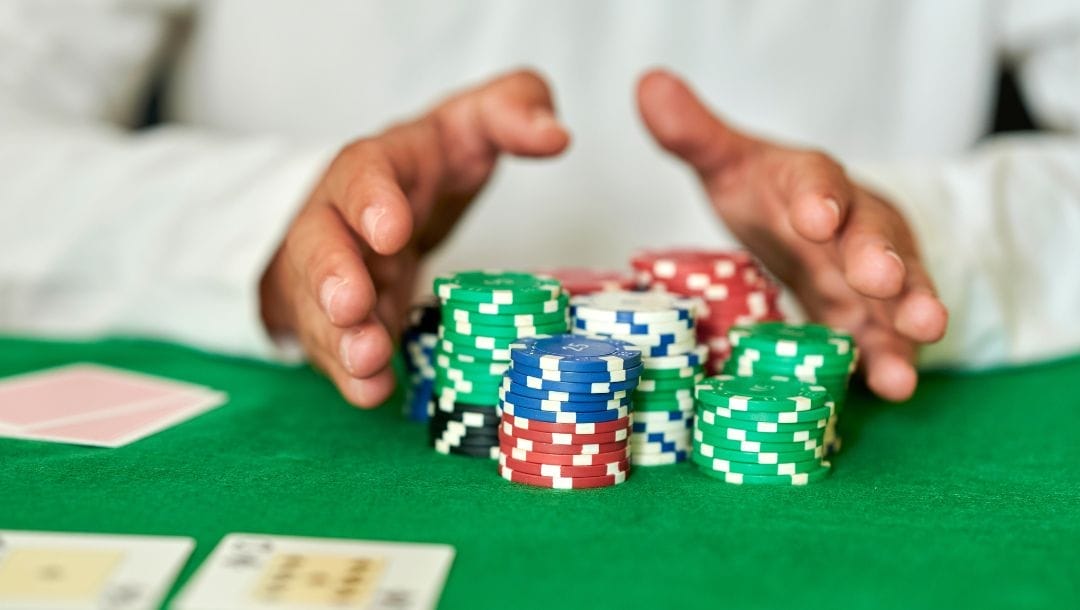 A person sitting at a poker table, pushing stacks of red, blue, green, white, and black poker chips forward.