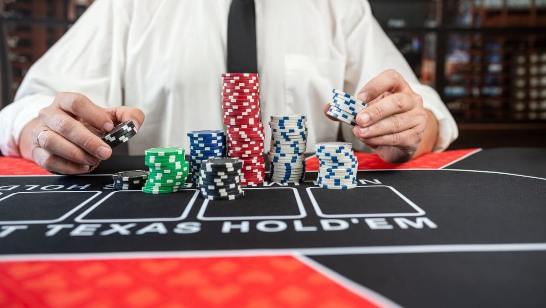 A person sitting at a poker table, with stacks of blue, red, green, white, and black poker chips in front of him.
