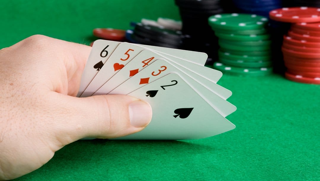A poker player lifts up their five hole cards. Their hand has a 6, 5, 4, 3, and 2.