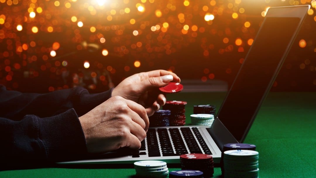 A man plays online poker on a laptop, surrounded by stacks of poker chips