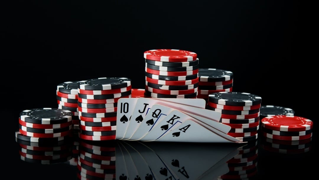 A royal flush in spades in front of stacks of red and black poker chips