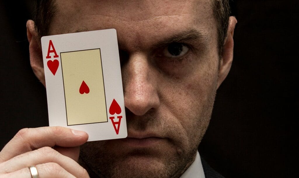 A man holds an ace of hearts in front of his left eye.