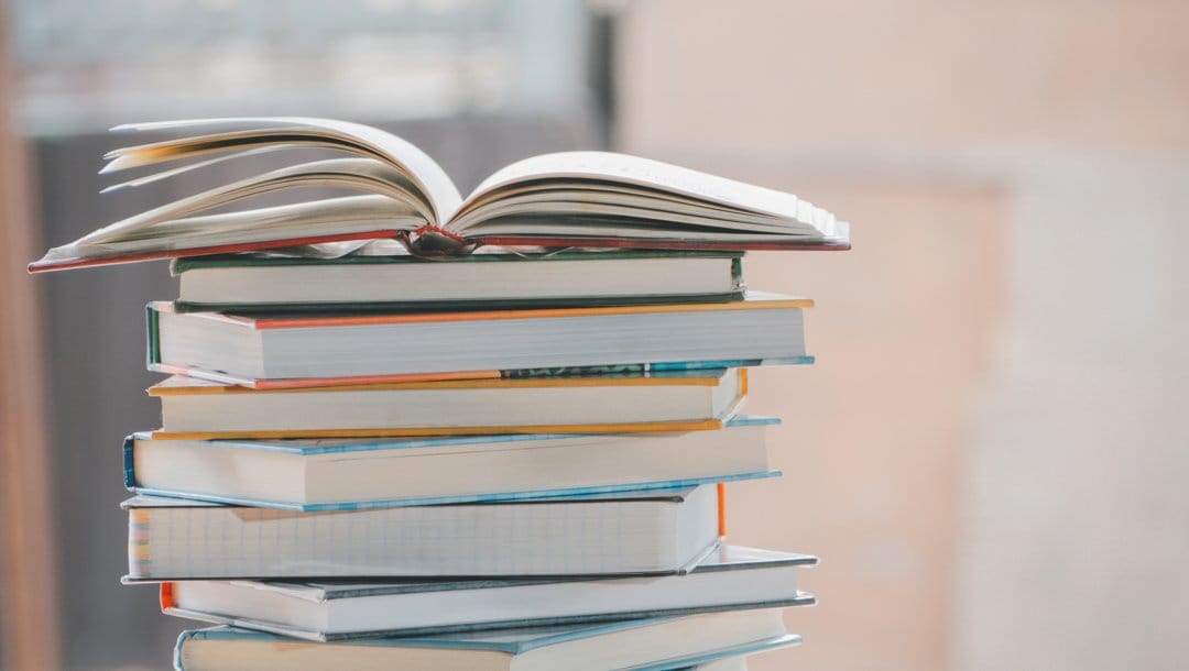 A stack of books on a table. The book on top of the stack is open.
