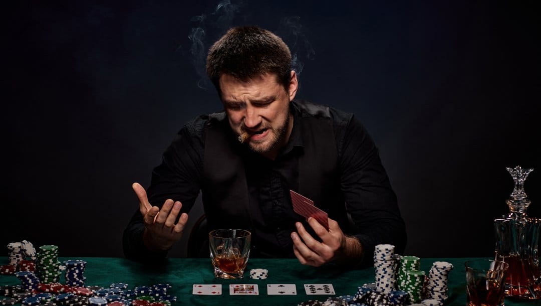 A poker player smoking a cigar looks down at the poker table in front of them, a look of frustration on their face.