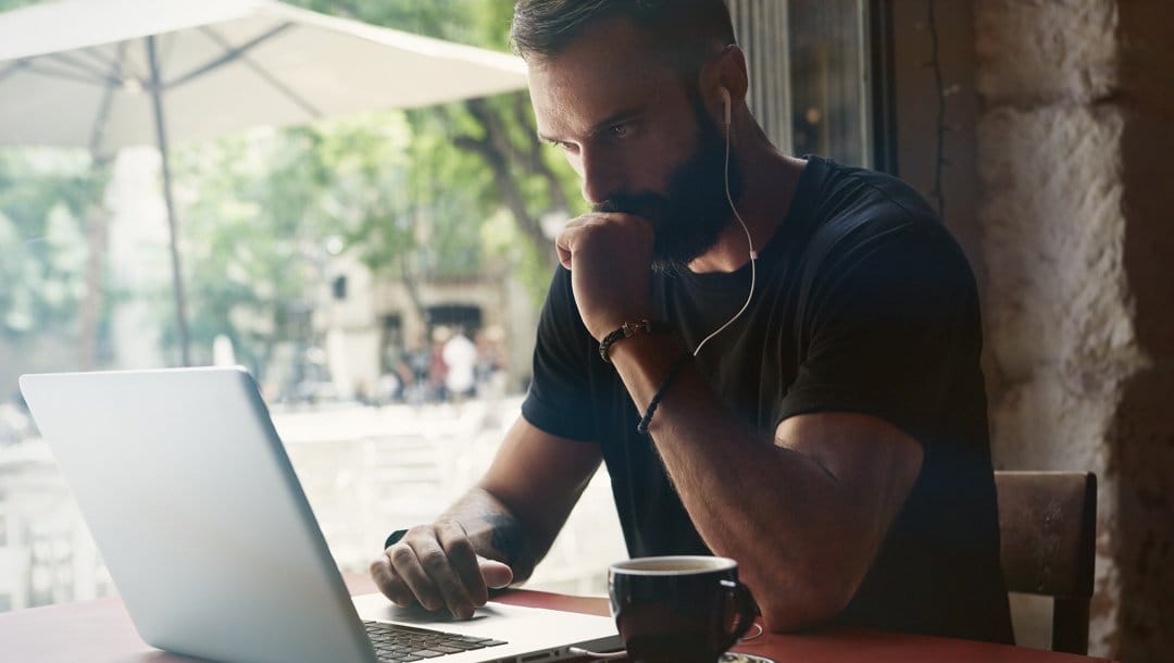 A person sits in front of their laptop at a coffee shop. They have their fist against their mouth while they concentrate.